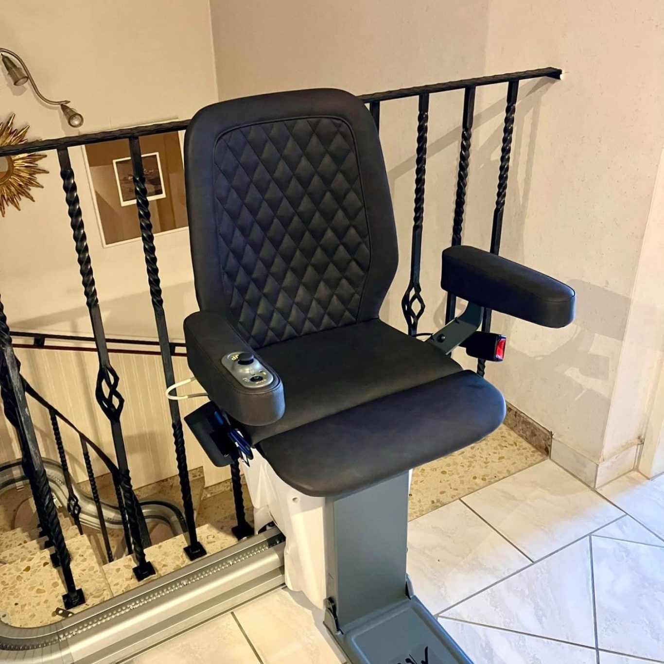 Treppenlift mit schwarzem Sitz und Armlehnen, montiert an einem Treppenabsatz.