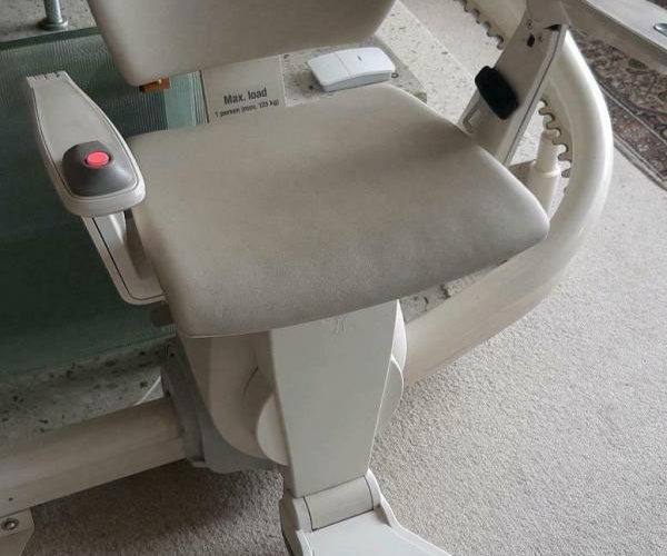 Ein beige Sitz mit Armlehnen auf einem Rollstuhl oder Pflegebett.